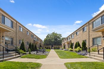 Beautifully landscaped courtyard at Monon Court Apartments in Broad Ripple, IN, with beige brick buildings and community green space close to Monon Trail access.